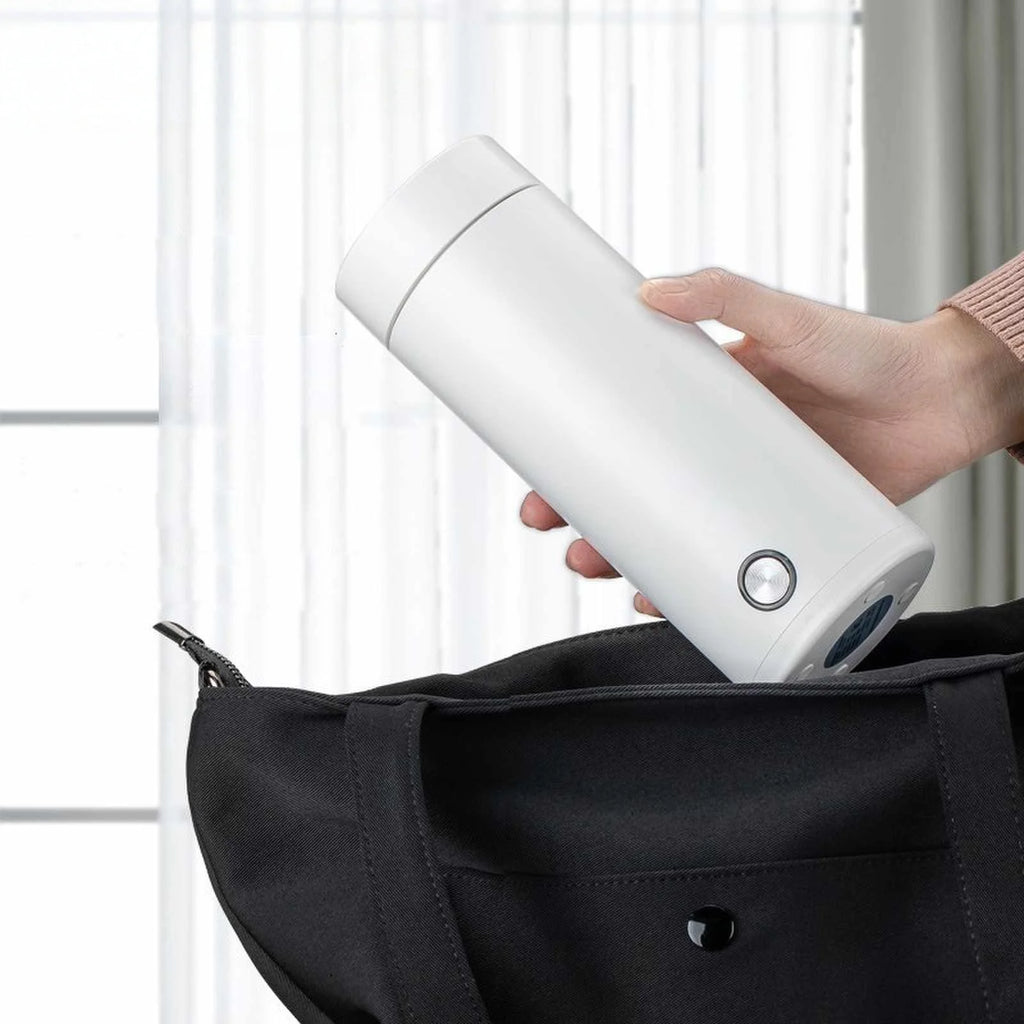Person holding a white cylindrical device next to a black bag.